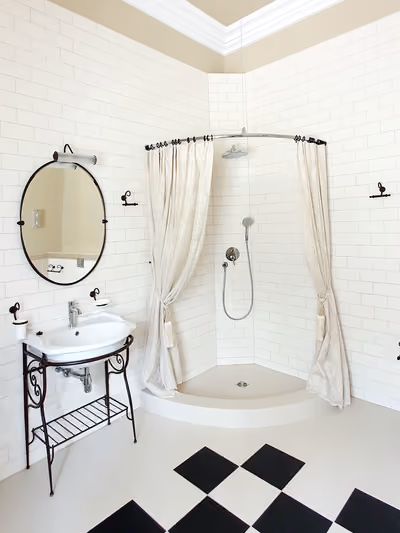 Small vintage-style bathroom with white subway-tile walls, a wrought-iron pedestal sink stand, an oval mirror, and a black-and-white diamond checkerboard tile floor