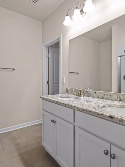 Renovated bathroom with a white double-sink vanity, granite countertop, brushed-nickel faucets, and a glass-enclosed subway-tile shower reflected in the mirror