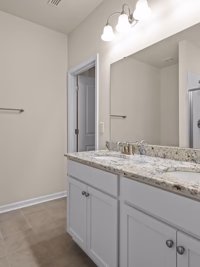 Renovated bathroom with a white double-sink vanity, granite countertop, brushed-nickel faucets, and a glass-enclosed subway-tile shower reflected in the mirror