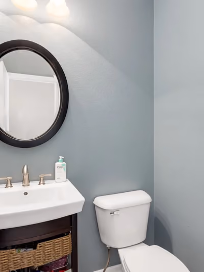 Modern powder room with slate-blue walls, a round black-framed mirror, and a floating white sink with brushed-nickel fixtures