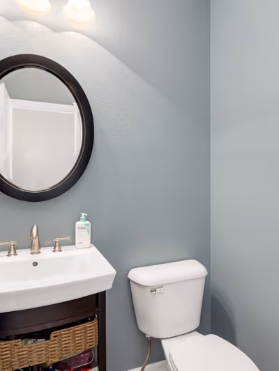 Modern powder room with slate-blue walls, a round black-framed mirror, and a floating white sink with brushed-nickel fixtures