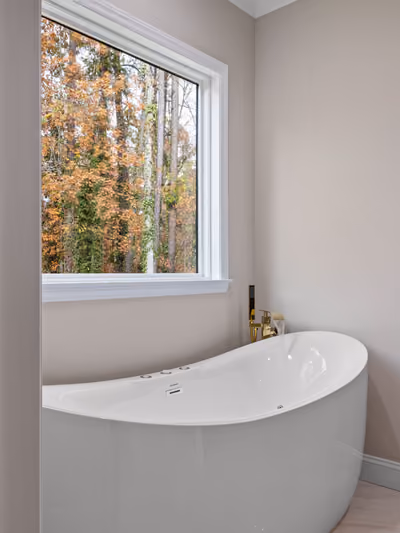 Freestanding oval soaking tub tucked into a corner beneath tall windows with white plantation shutters, framed by white marble subway-tile wainscoting