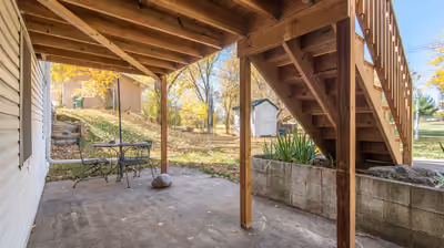 Underside of a raised wood deck showing its post, beam, and joist framing alongside a built stairway