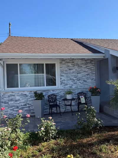 Renovated single-story home exterior with gray stacked-stone accent siding, new windows, a paver patio, and fresh landscaping