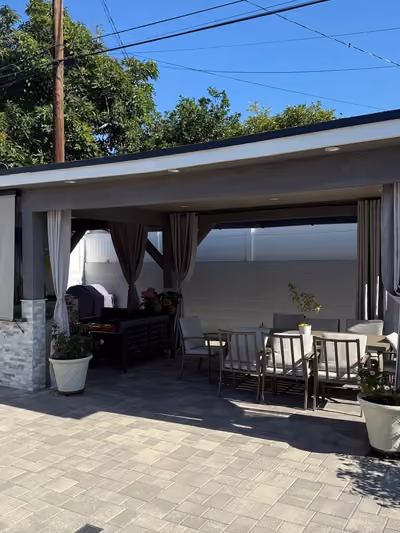 Custom outdoor patio cover with stone-clad support columns, retractable shade curtains, and an outdoor dining set