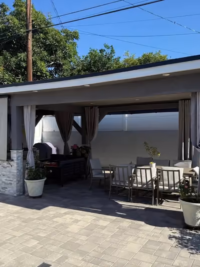 Custom outdoor patio cover with stone-clad support columns, retractable shade curtains, and an outdoor dining set