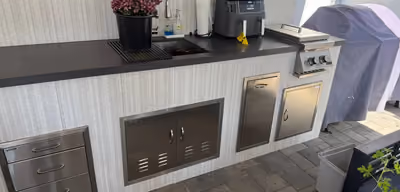 Outdoor kitchen counter with a sink, stainless steel storage cabinets, and a countertop air fryer next to a covered grill