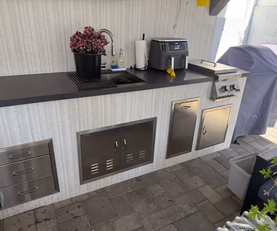 Outdoor kitchen counter with a sink, stainless steel storage cabinets, and a countertop air fryer next to a covered grill
