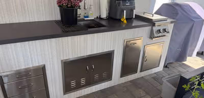 Outdoor kitchen counter with a sink, stainless steel storage cabinets, and a countertop air fryer next to a covered grill