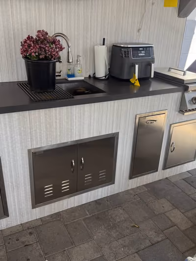Outdoor kitchen counter with a sink, stainless steel storage cabinets, and a countertop air fryer next to a covered grill