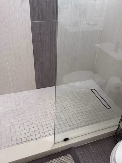 Walk-in glass shower with light gray hexagonal mosaic floor tile and gray plank-style wall tile