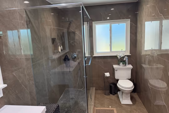 Renovated bathroom with a glass-enclosed shower, pedestal toilet, and glossy brown marble-look tile walls and floor