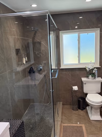 Renovated bathroom with a glass-enclosed shower, pedestal toilet, and glossy brown marble-look tile walls and floor