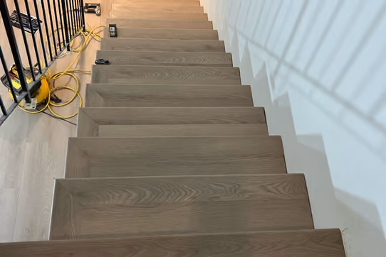Staircase mid-installation with new wood-look laminate flooring on the treads, tools and extension cords visible