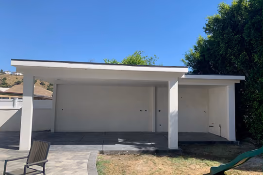 Exterior of a newly built stucco patio cover/carport structure with white trim and a flat roof