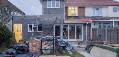 Home addition mid-construction with new block walls, scaffolding, and a roofline tying into the original house