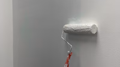 Paint roller applying a fresh coat of white paint to an interior wall