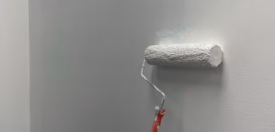 Paint roller applying a fresh coat of white paint to an interior wall
