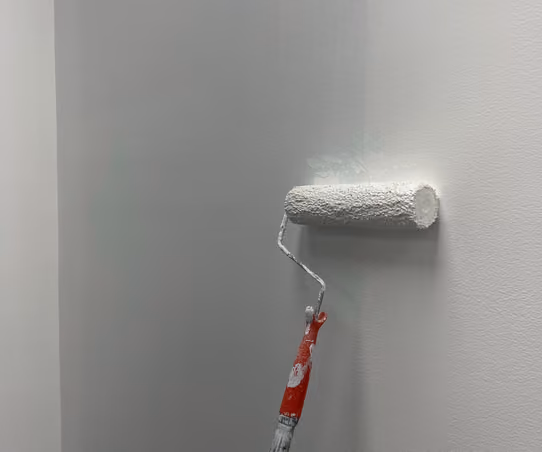 Paint roller applying a fresh coat of white paint to an interior wall