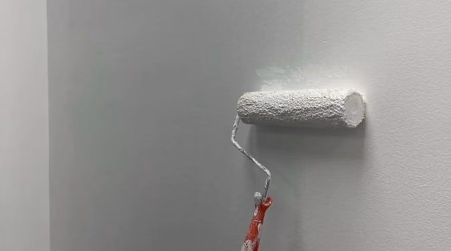 Paint roller applying a fresh coat of white paint to an interior wall