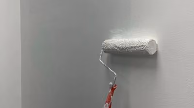 Paint roller applying a fresh coat of white paint to an interior wall