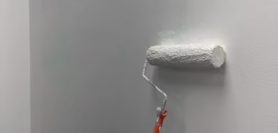 Paint roller applying a fresh coat of white paint to an interior wall