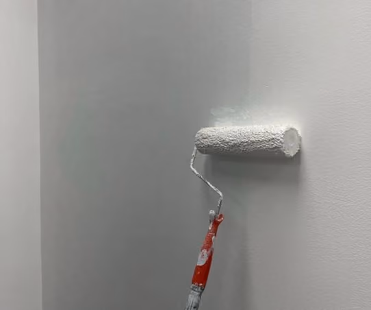 Paint roller applying a fresh coat of white paint to an interior wall