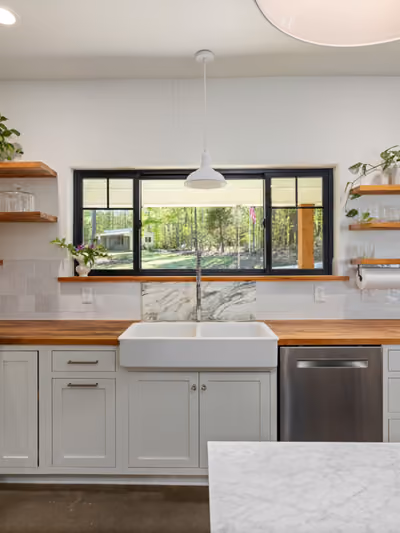 Farmhouse-style kitchen with white shaker cabinets, an apron-front farmhouse sink, butcher-block countertops, subway tile backsplash, and open wood shelving displaying dishware