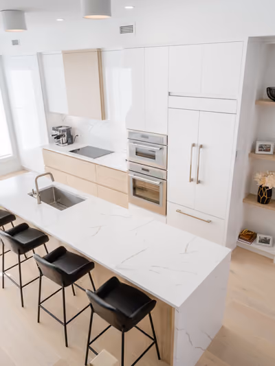 Modern kitchen with white flat-panel cabinetry, light oak accents, and a large quartz island featuring a waterfall-edge side panel