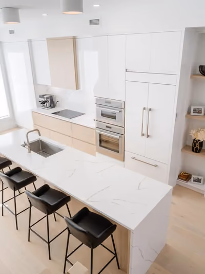 Modern kitchen with white flat-panel cabinetry, light oak accents, and a large quartz island featuring a waterfall-edge side panel