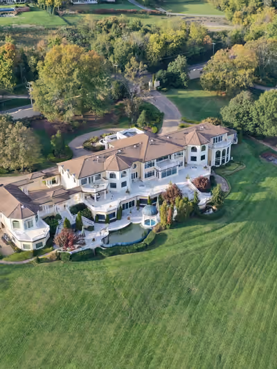 Aerial view of a sprawling tile-roofed estate home with a circular motor court, gated entrance, and expansive manicured grounds