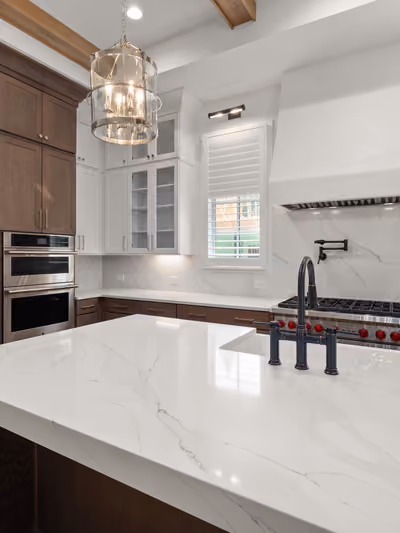 High-end kitchen with a large quartz waterfall island, professional gas range with pot filler, custom dark wood cabinetry, and a marble slab backsplash