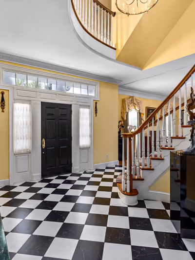 Grand entry foyer with a curved wooden staircase, black-and-white checkerboard marble floor, and a crystal chandelier