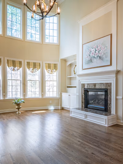 Two-story great room with a wall of tall arched windows, a marble fireplace flanked by built-in cabinetry, and rich hardwood flooring