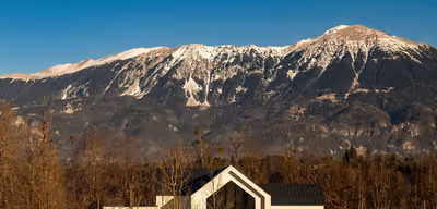 Modern luxury home with a dramatic glass gable against snow-capped mountains
