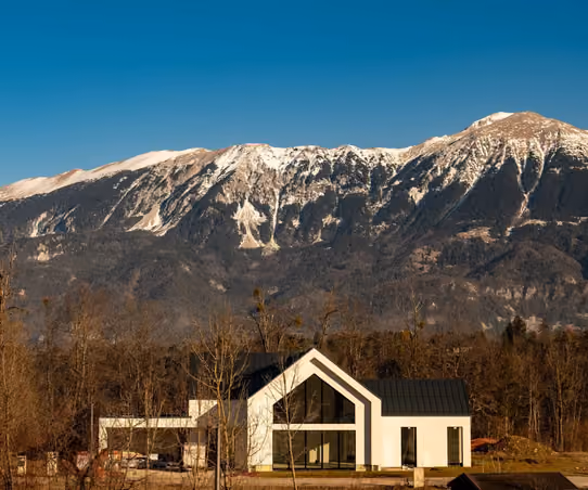 Modern luxury home with a dramatic glass gable against snow-capped mountains