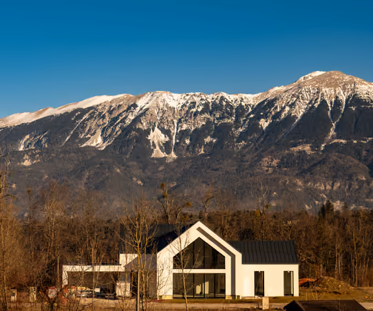 Modern luxury home with a dramatic glass gable against snow-capped mountains
