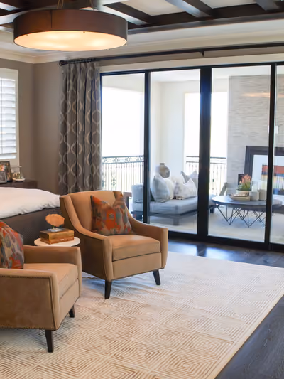 Spacious primary bedroom suite with a tufted leather headboard, coffered wood-beam ceiling, and sliding glass doors opening to a private balcony sitting area