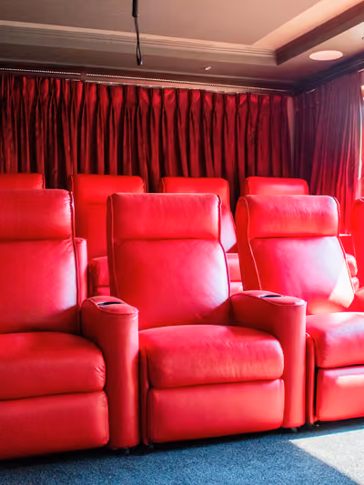 Dedicated home theater room with rows of red leather reclining seats and heavy red drapery along the walls