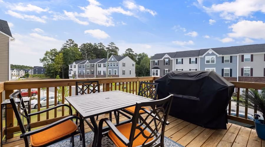 Elevated backyard wood deck with a dining table, chairs, and a covered gas grill