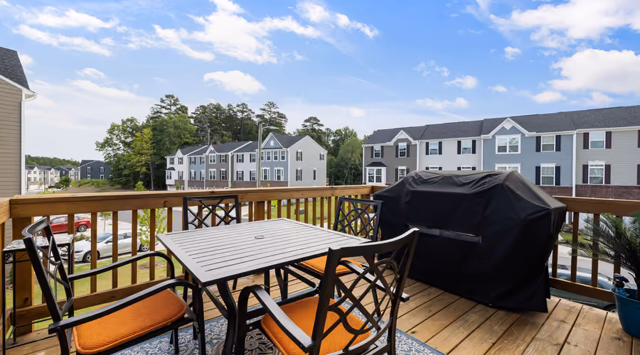 Elevated backyard wood deck with a dining table, chairs, and a covered gas grill