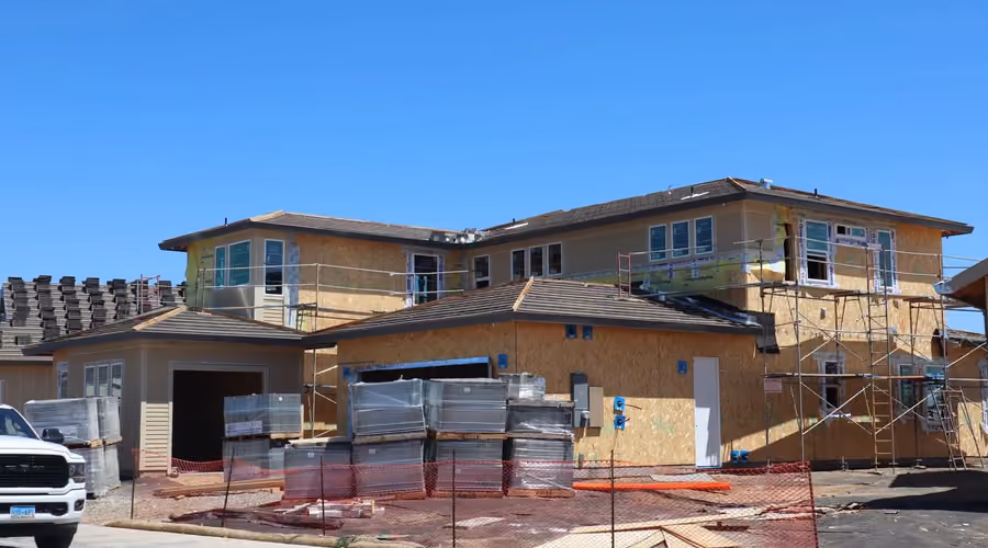 Two-story home under construction with a second-story addition against a blue sky