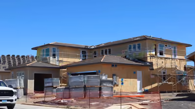 Two-story home under construction with a second-story addition against a blue sky