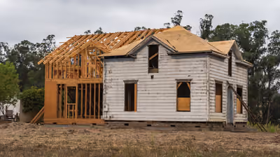 Existing house with a new timber-framed wing and roof structure being built onto it as a home addition