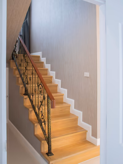 Renovated staircase with light oak wood treads, white risers and trim, and a new dark wrought-iron railing topped with a wood handrail